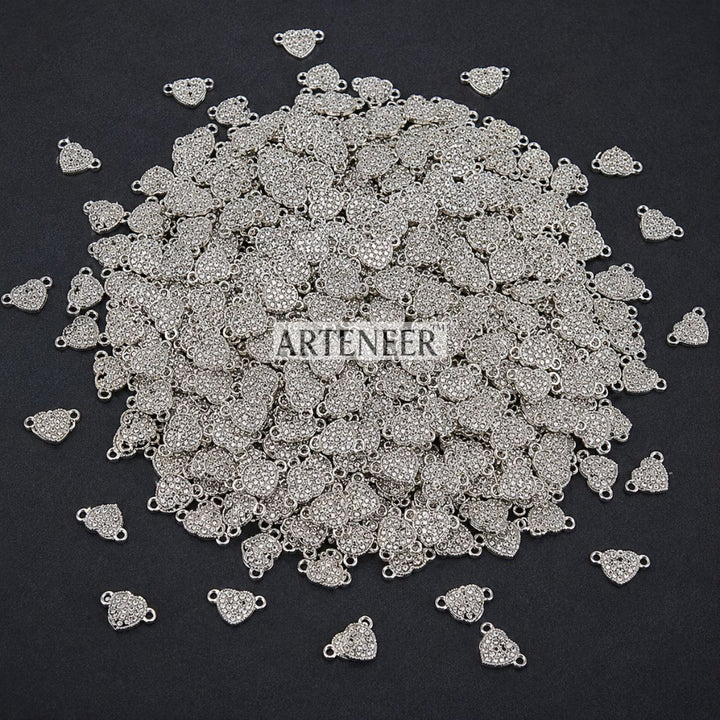 Pile of silver jewelry charms with 'Arteneer' branding on a black background