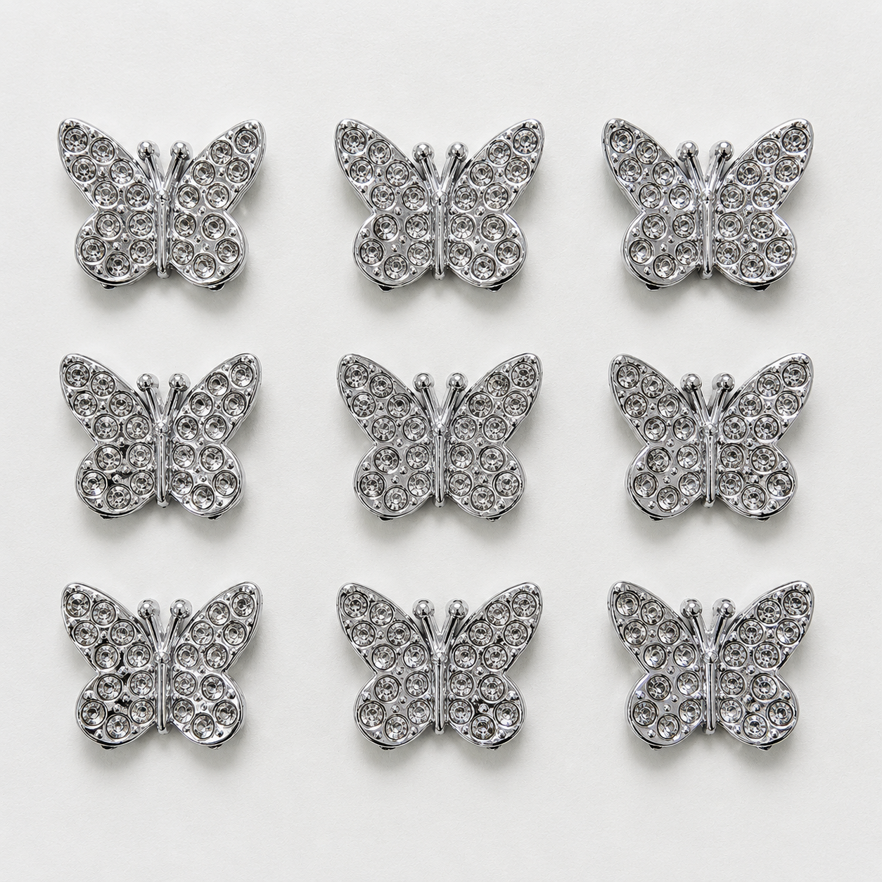 Silver butterfly-shaped decorative items with rhinestones on a white background