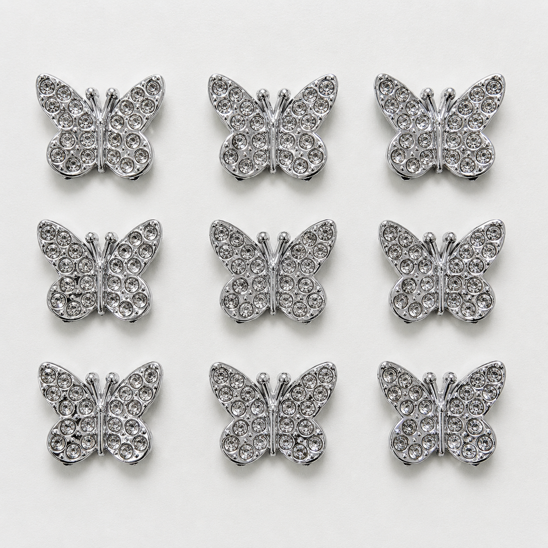 Silver butterfly-shaped decorative items with rhinestones on a white background