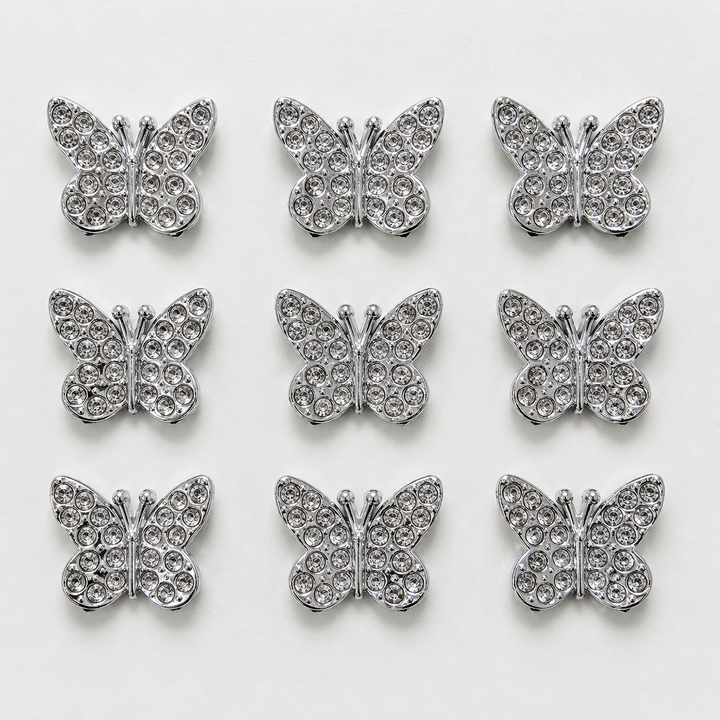 Silver butterfly-shaped decorative items with rhinestones on a white background